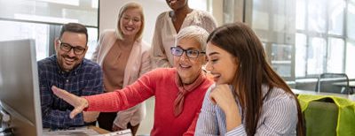 old woman in pink sweater happily pointing to computer screen showing a group of people