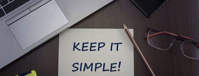 post it note on desk that says "Keep it simple!" surrounded by office supplies